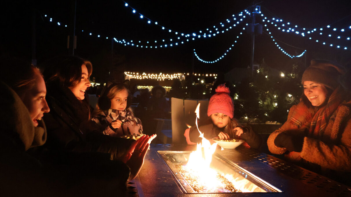 A family sitting around a fire pit, warming their hands and snacking on popcorn.