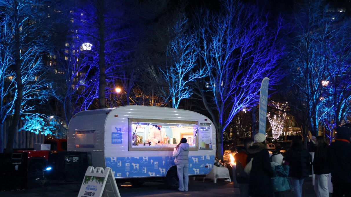 A white truck selling hot beverages in front of a display of blue lit up trees.