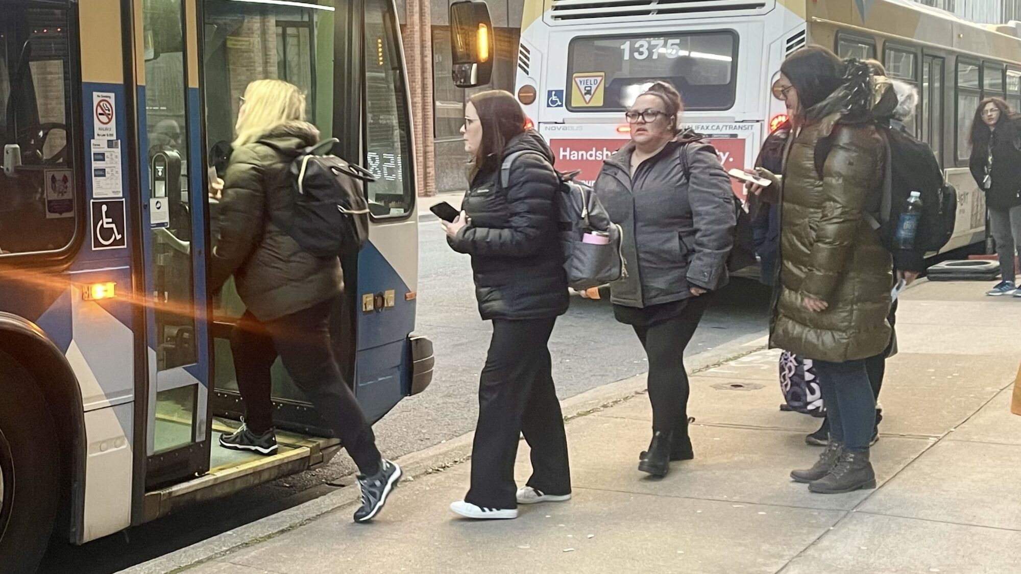 Four people are lined up to board a Halifax Transit bus. The person at the front of the line is stepping on to the bus.