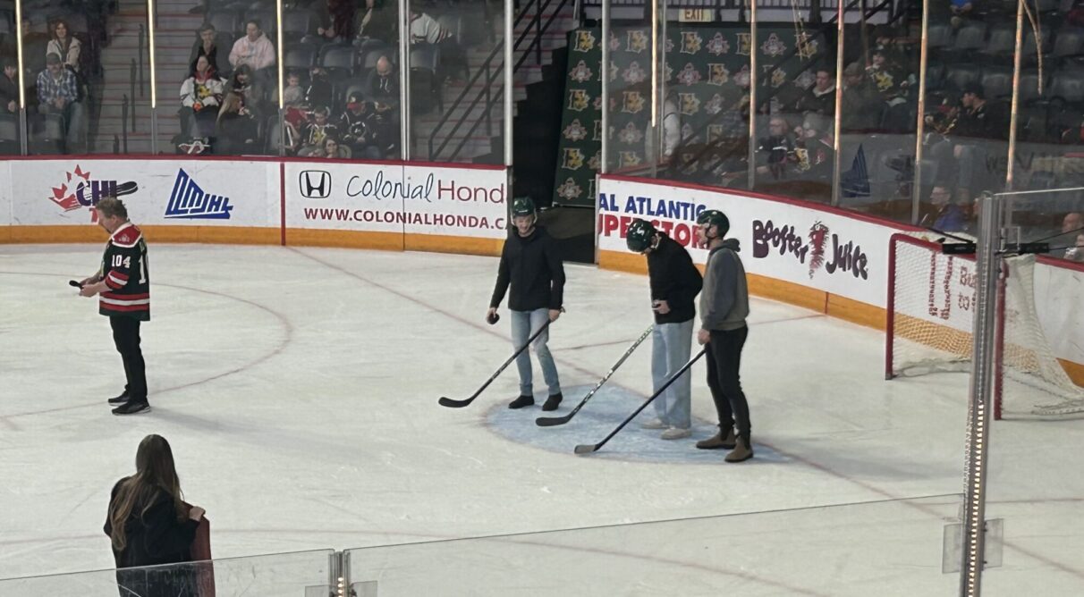 Three men with hockey helmets and sticks stand in the ice at the Scotiabank Centre