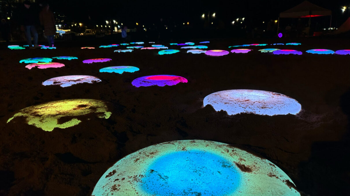 Colourful light up pads in the sand with people jumping on them in the distance