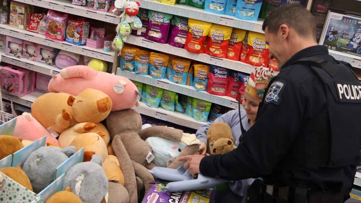 A police officer and a kid look at a large pile of stuffed animals.