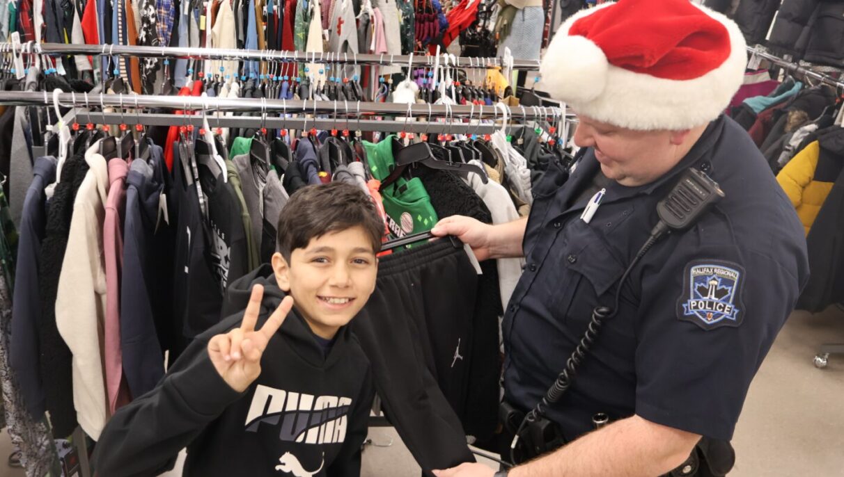 A police officer wearing a Santa hat shows a pair of Jordan brand pants to a young boy showing a peace sign to the camera.