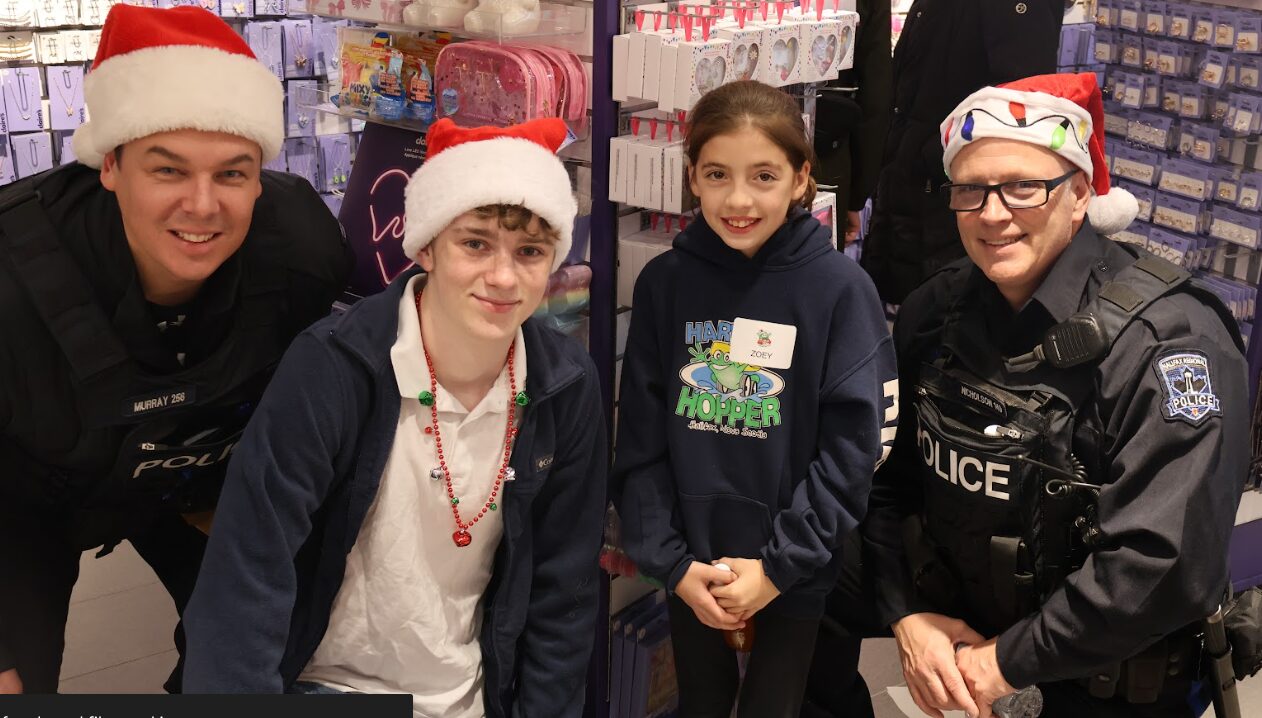 Two policemen wearing Santa hats pose with two kids, one of them is wearing a Santa hat.