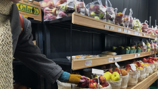 A person's hand selects apples in a grocery store.