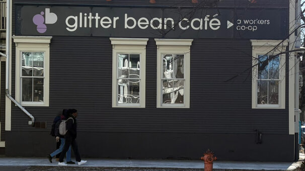 Three people walk beneath a sign that says "glitter bean cafe."