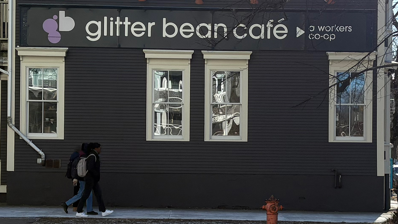 Three people walk beneath a sign that says "glitter bean cafe."