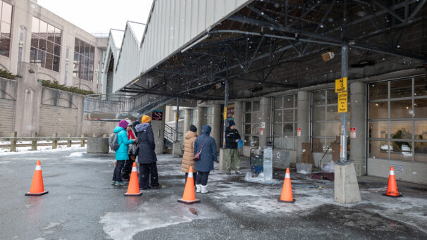 a crowd gathers around an ice block as they watch a man prep it for carving using power tools