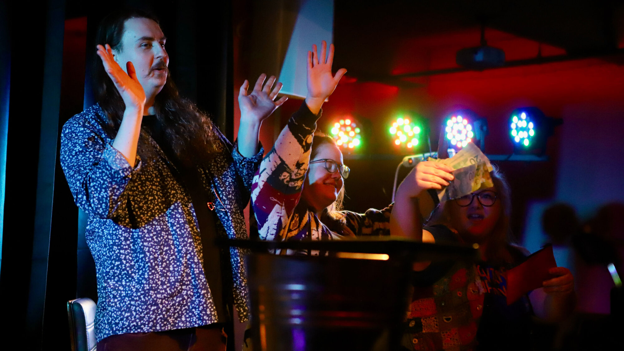 Two people raise their hands in a bar lit with event lights