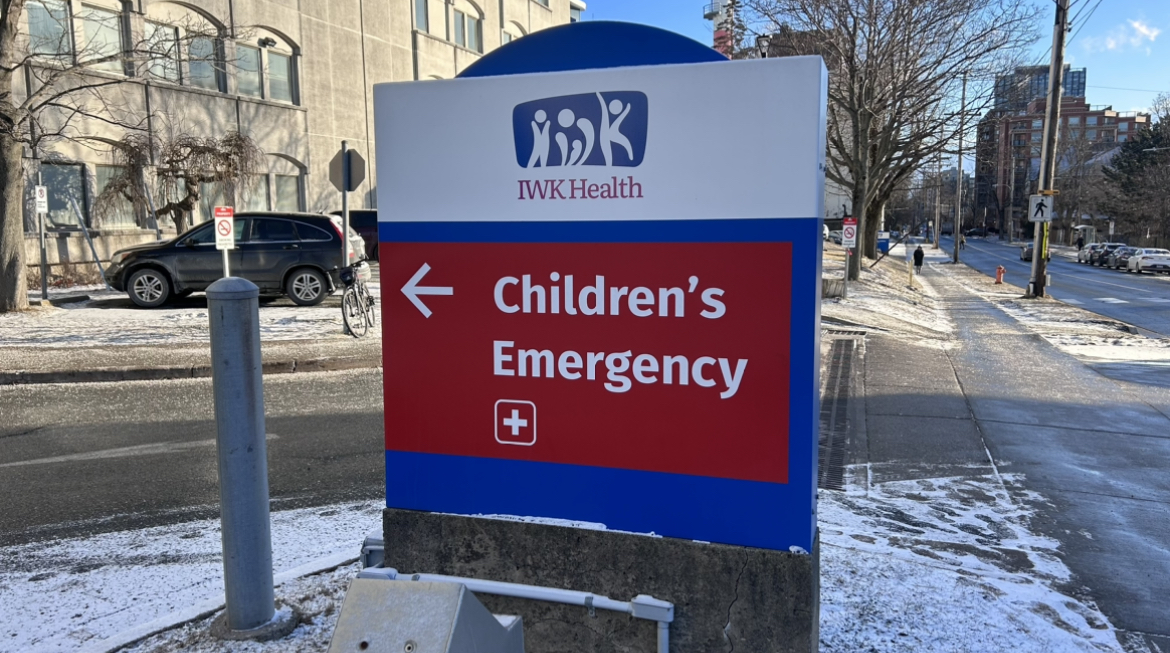 An IWK Health sign with snow on the ground around it. The bottom of the sign is in red and points to the Childrens Emergency Department.