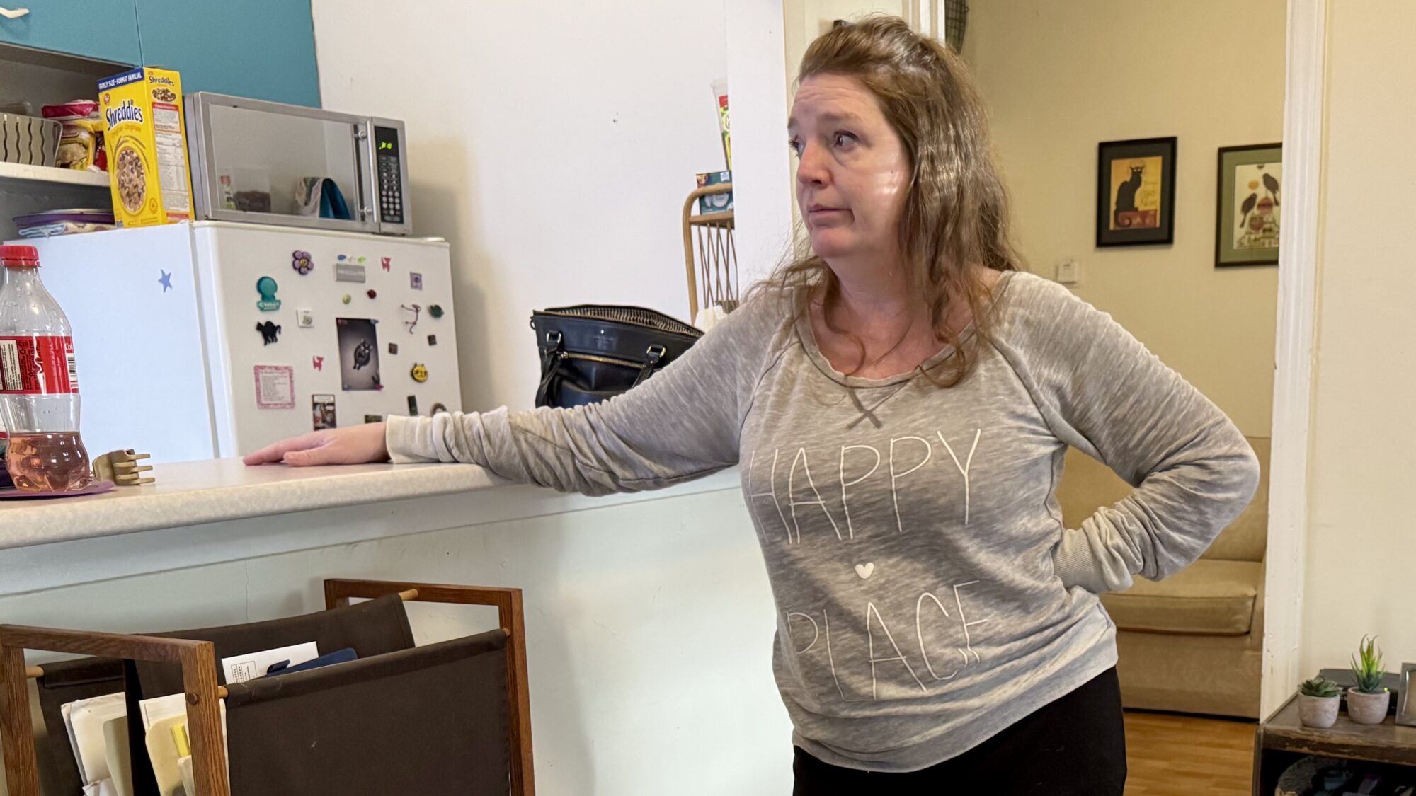 Woman leans on kitchen counter and gazes at her home.