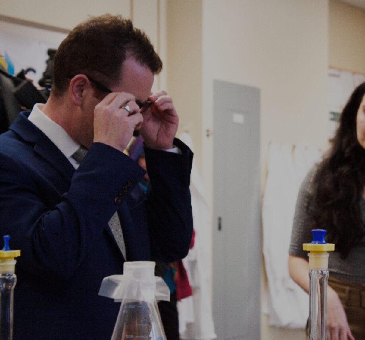 A man in a blue suit tries on glasses in a lab.