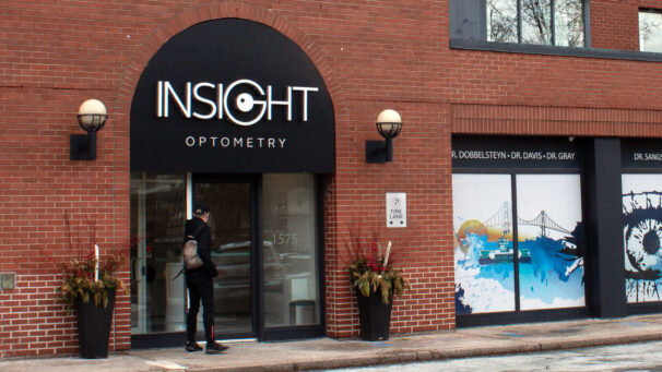 A person is about to open the door at Insight Optometry. It's a brick building with glass doors and an arched sign.