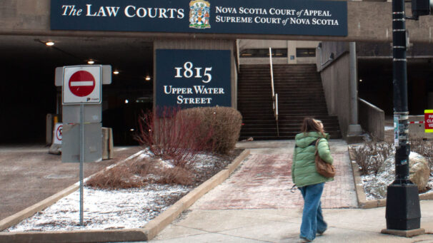 A person in a green coat walks by the law courts building on Upper Water St. The street facing sign is blue with white text.