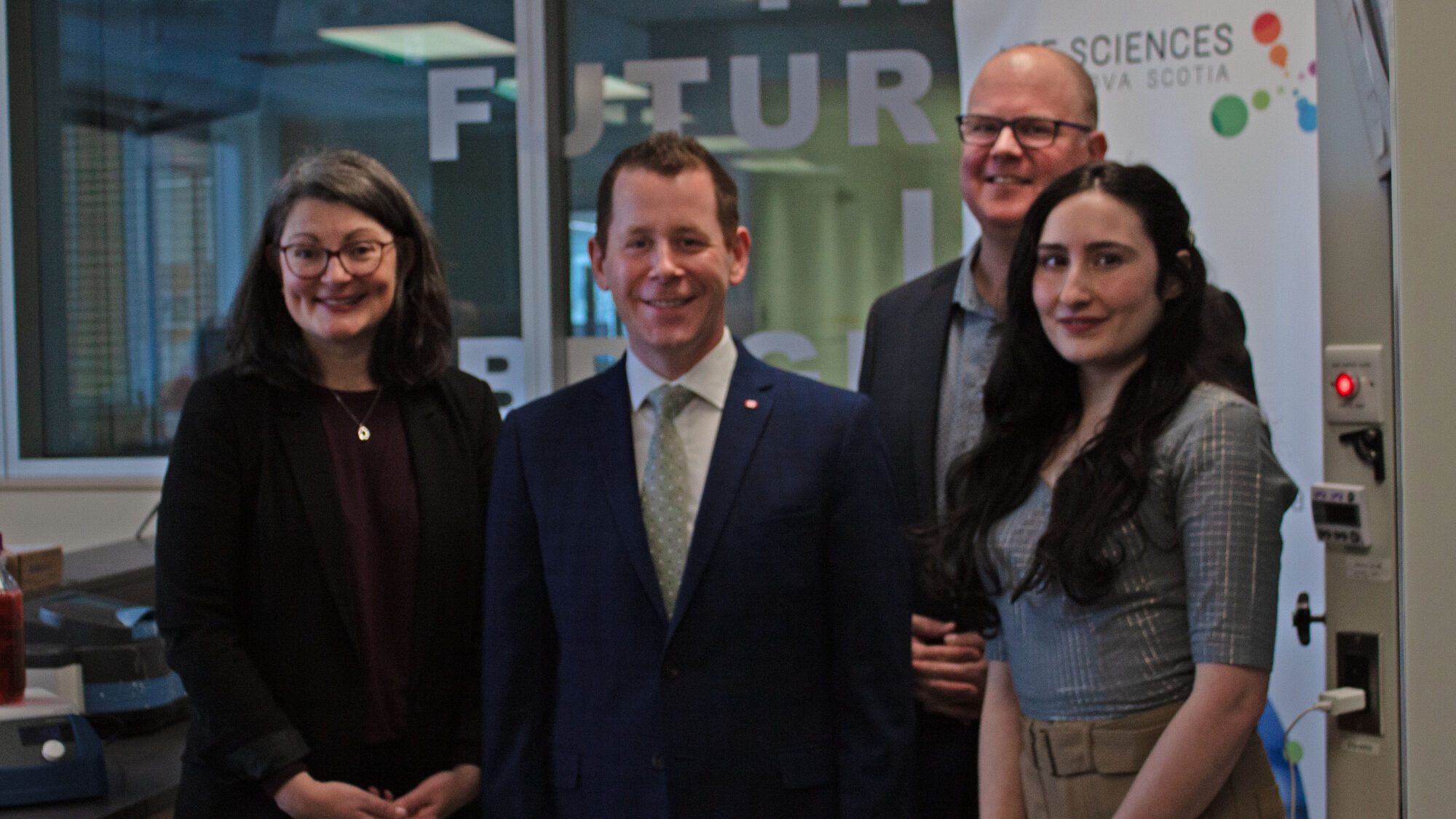 Four people pose for a photo in front of a glass wall.