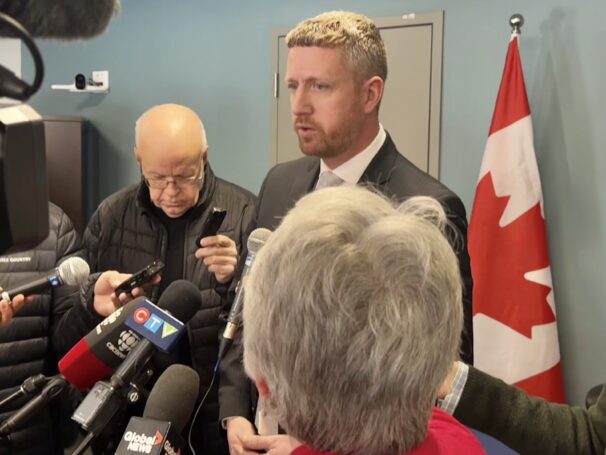 A man wearing a grey suit answer questions from reporters.