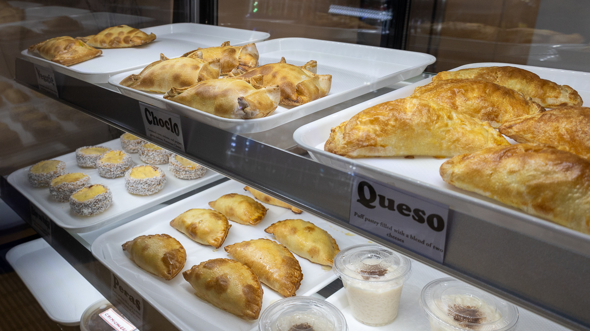 Empanadas, a dinner pastry shaped like a half moon and golden brown, sit in white trays inside a glass display case.