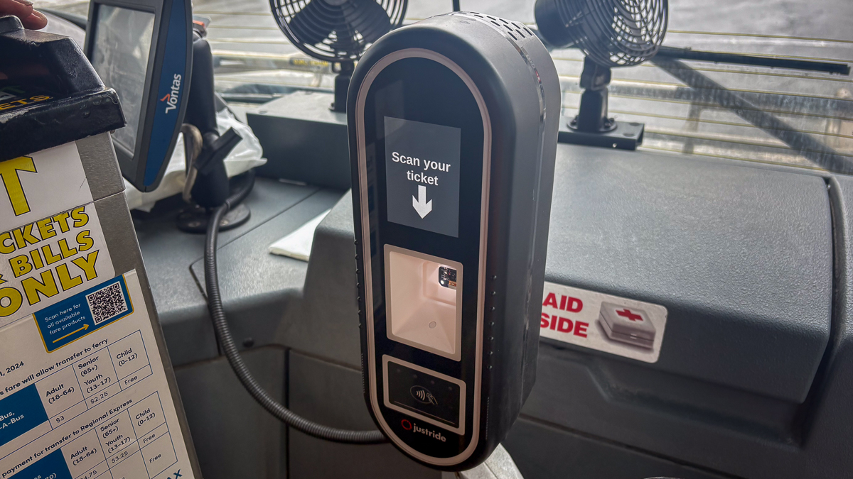 A black oval shaped ticket scanner inside a Halifax transit bus. the screen reads "scan your ticket" with an arrow pointing down towards the scanner.