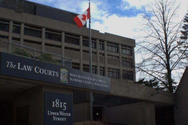 The front of the Nova Scotia Supreme Court building. The sky is blue and there's a Canadian flag flying.