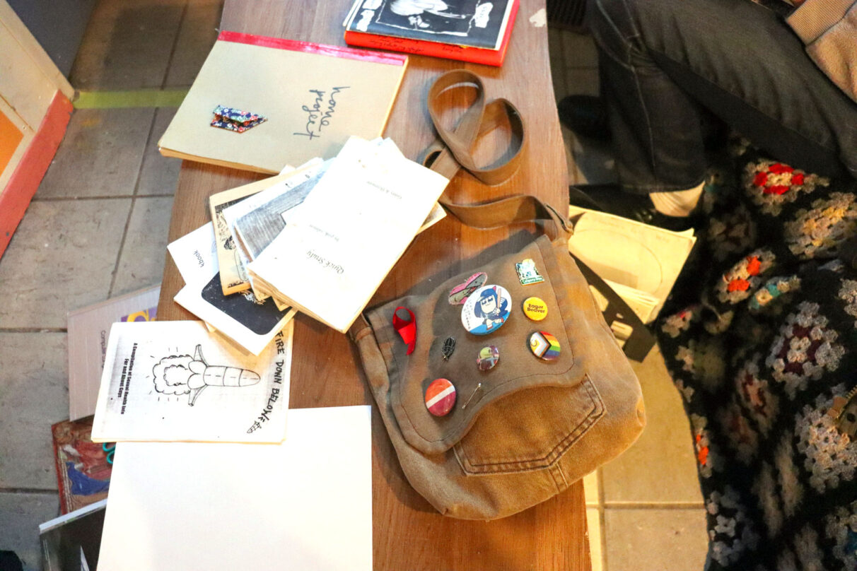 Zines sit on a coffee table along with a brown satchel decorated with various pins in the Anchor Archive Zine Library on Gottingen Street in Halifax, Nova Scotia on September 22, 2025. The zines are being made during the weekly zine-making drop-in.