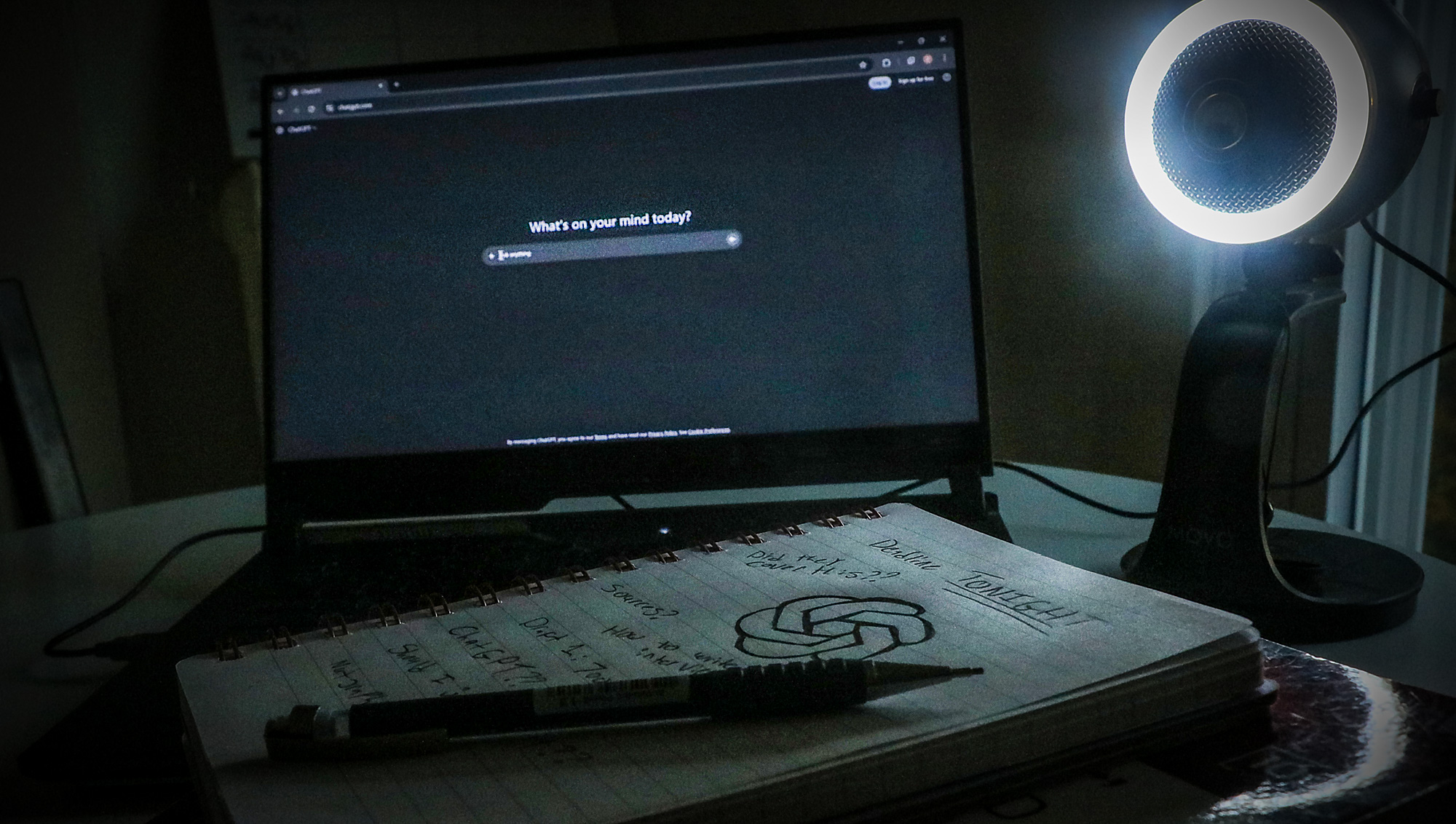 A laptop displaying ChatGPT sits open on a table beside a notebook and journalism textbooks.