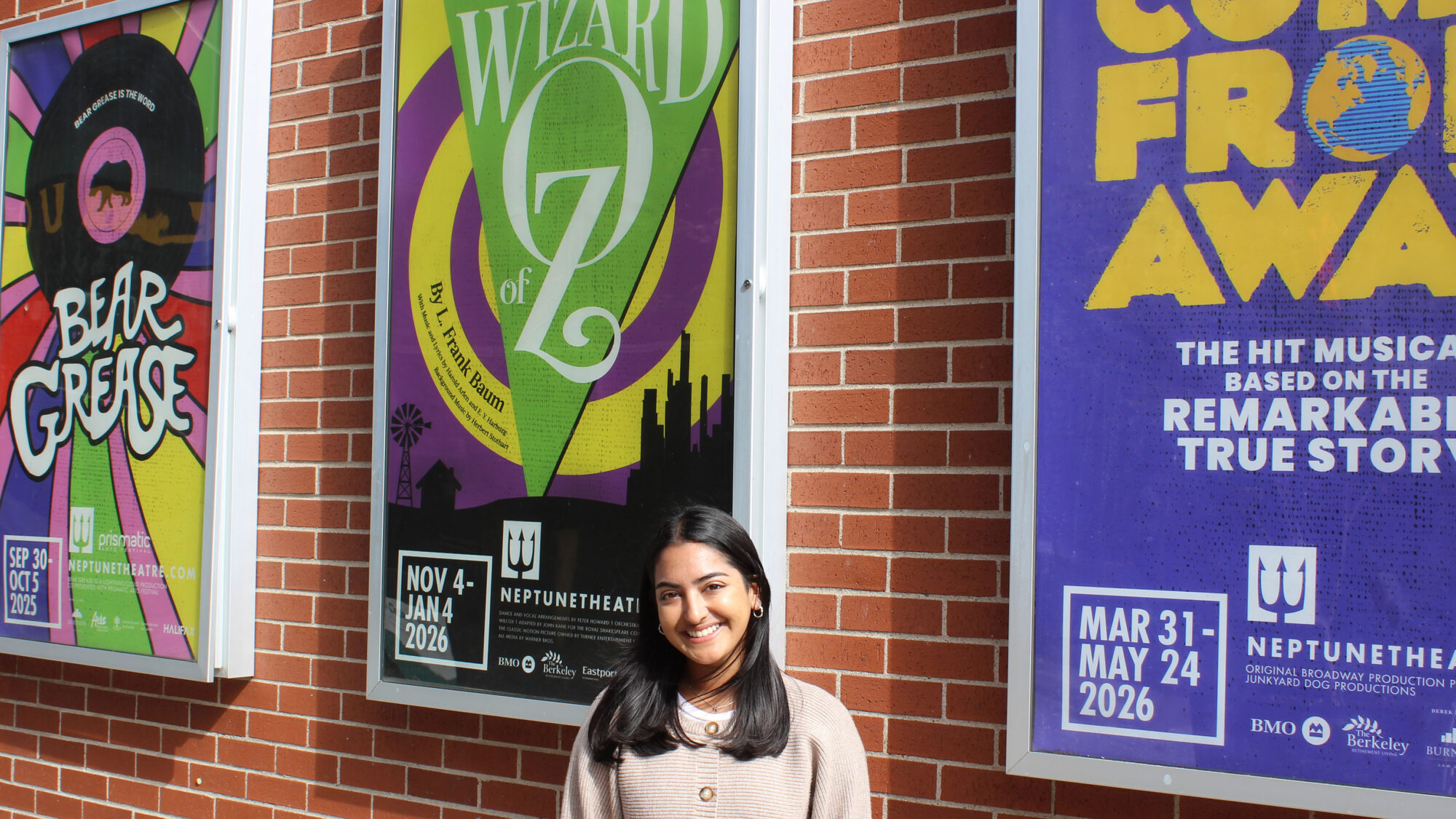 Henna Matharu standing with Wizard of Oz poster outside of Neptune Theatre.