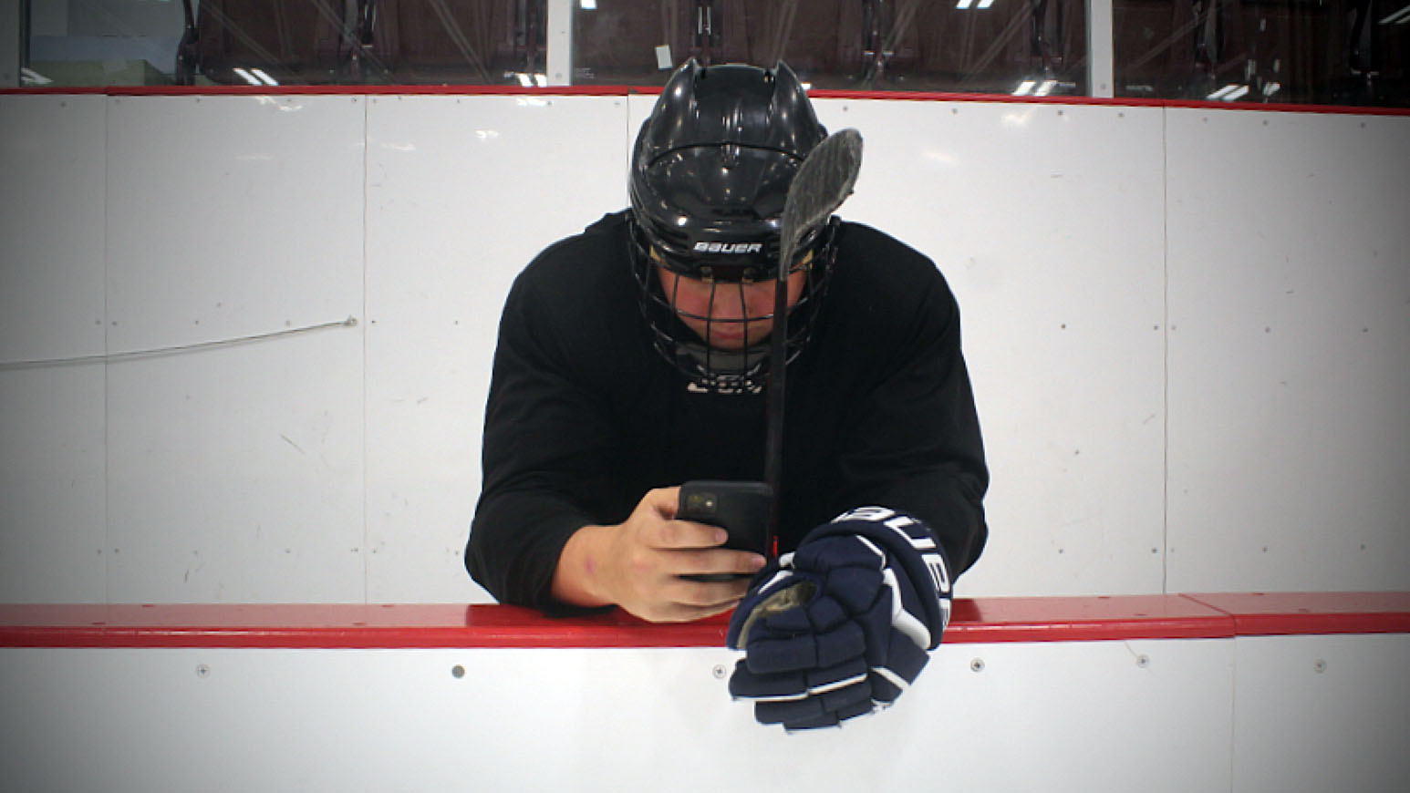 Instead of hitting the ice, a hockey player sits on the bench distracted by social media on their phone.