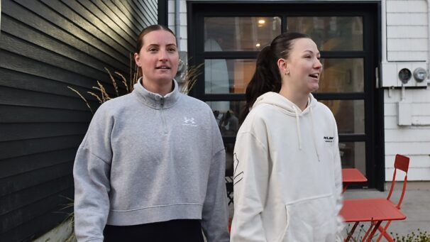 Two women standing next to each other. The women on the right is mid conversation.