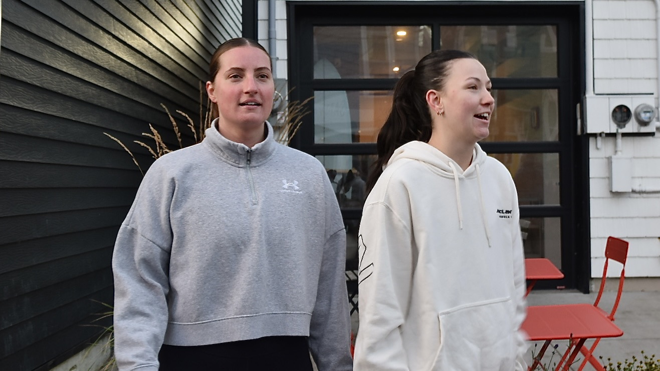 Two women standing next to each other. The women on the right is mid conversation.