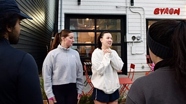 Two women standing next to each other. The women on the right is mid conversation.