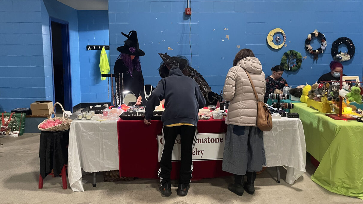 Two people standing in front of a table, with their backs against the camera. Looking at product for sale.