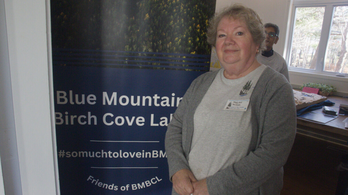 A woman stands in front of a sign that says Blue Mountain Birch Cove Lakes