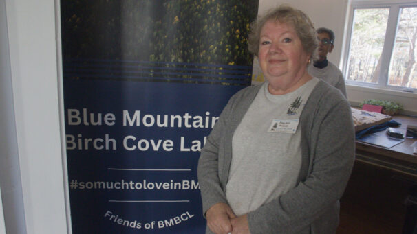 A woman stands in front of a sign that says Blue Mountain Birch Cove Lakes