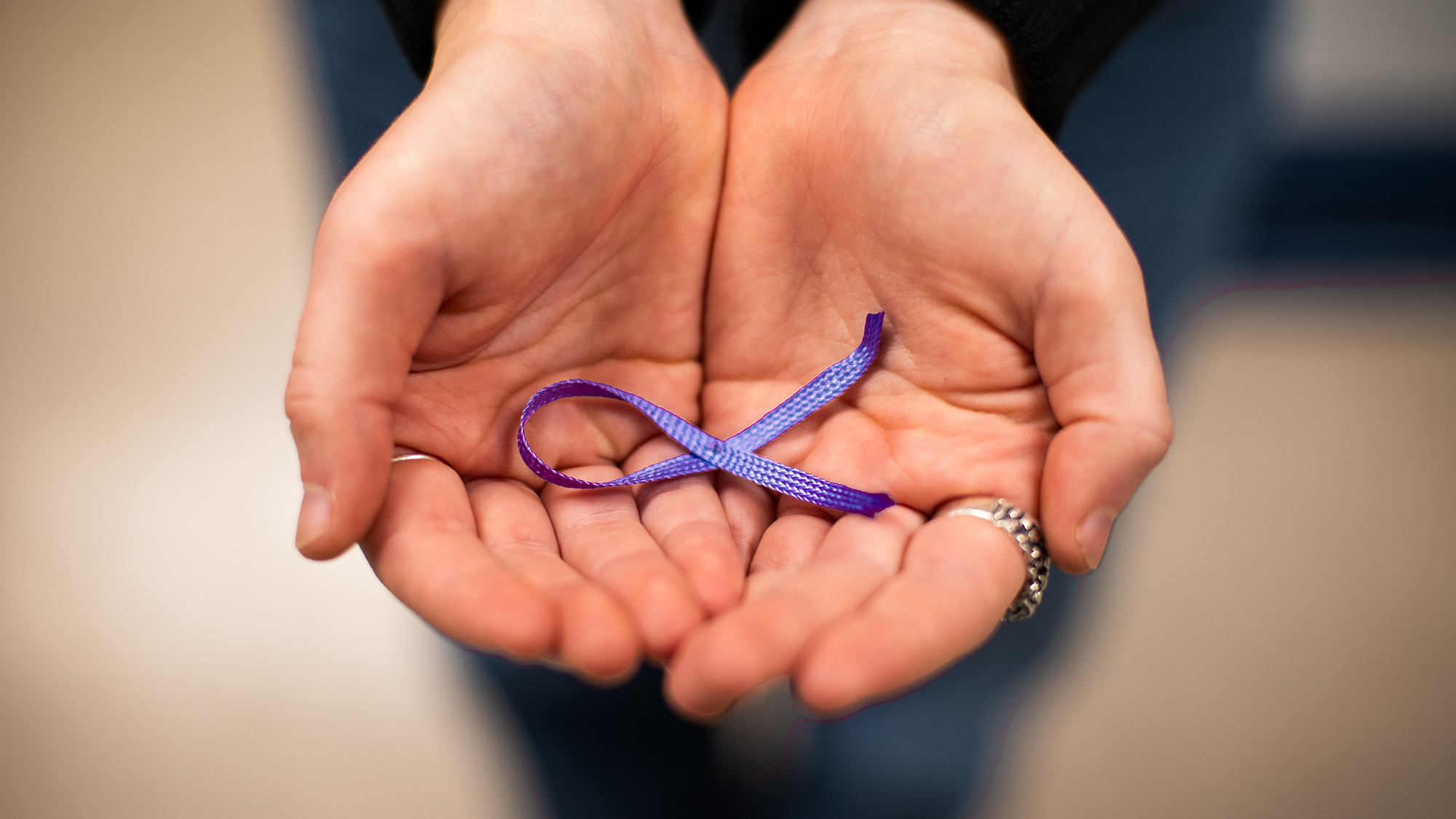 Two hands holding a purple ribbon