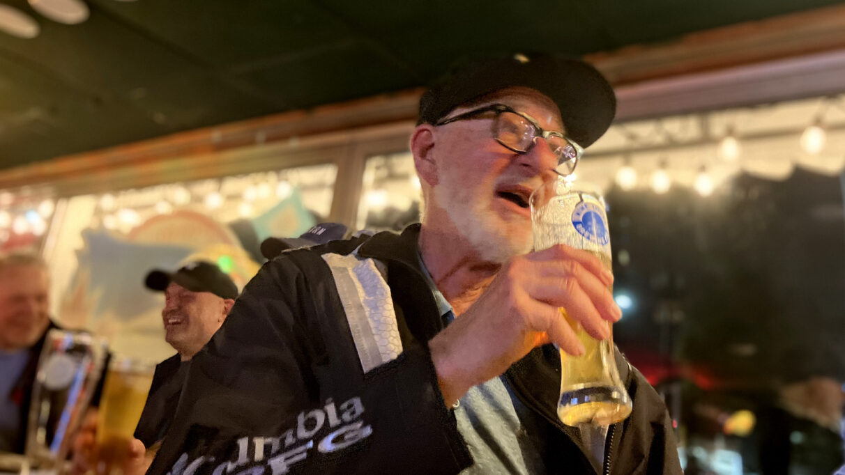 A man in a black jacket with a glass a beer.