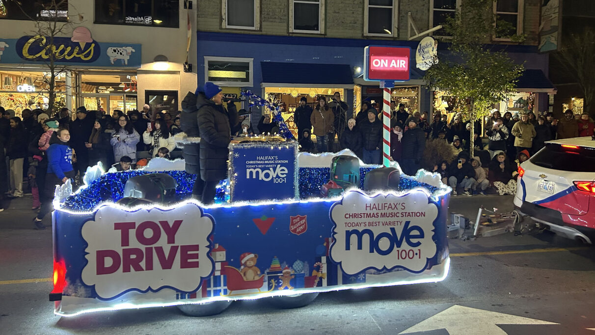 Parade toy drive float drives on the street in front of a crowd.