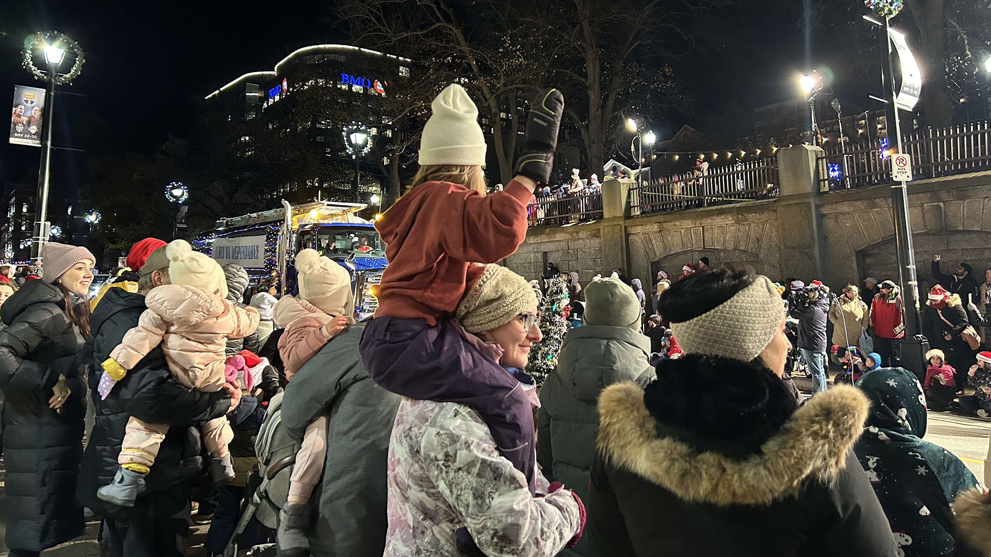 Child sitting on women's shoulders in a crowd of people watching the parade.