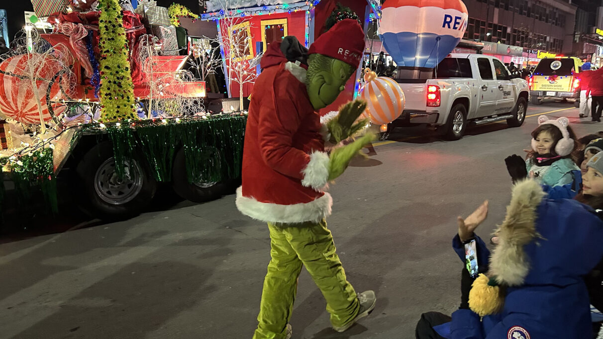 A Grinch costume waving to a crowd of children.