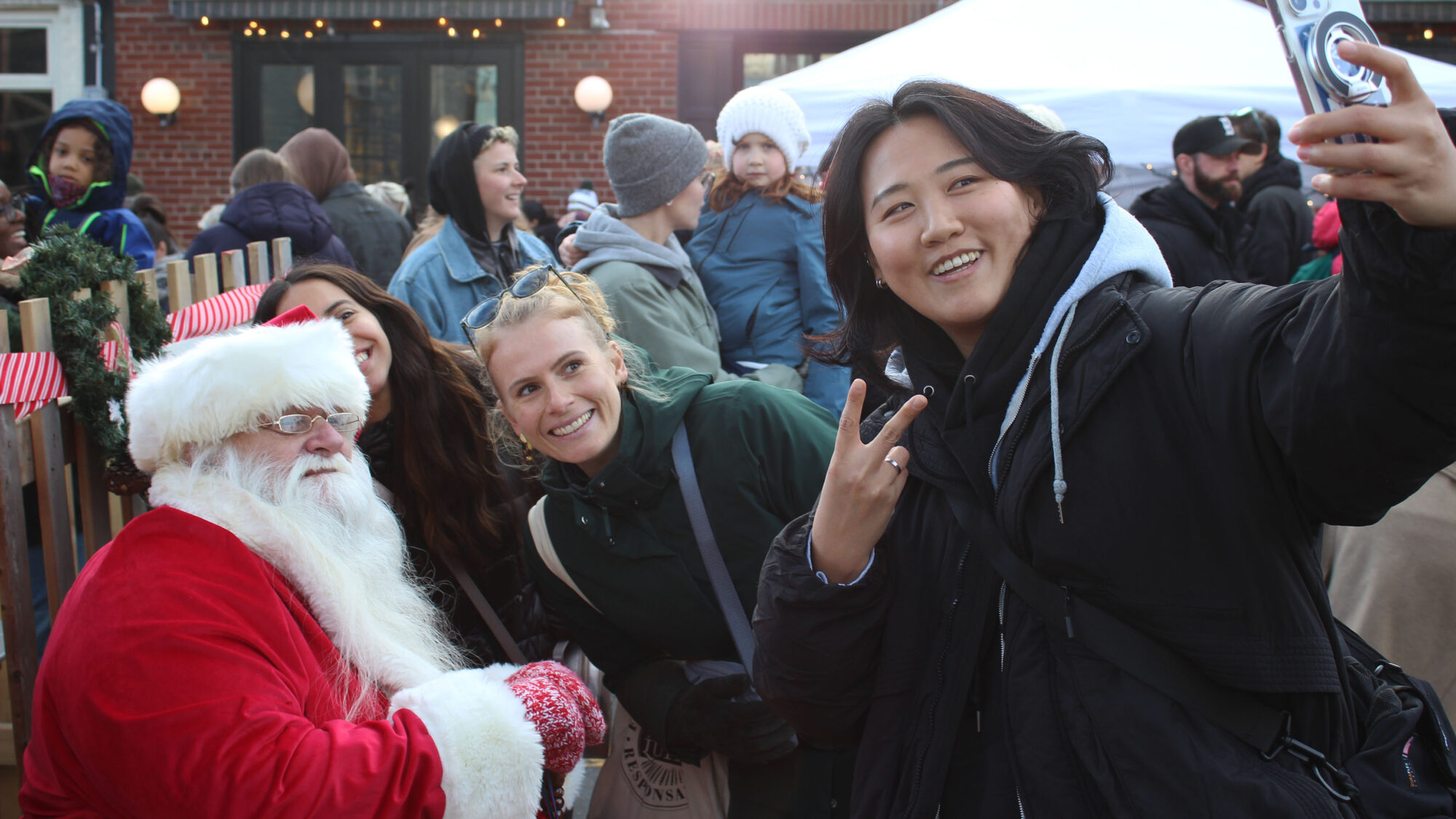 Three people taking a selfie with Santa Claus at the Agricola Street Holiday Market.