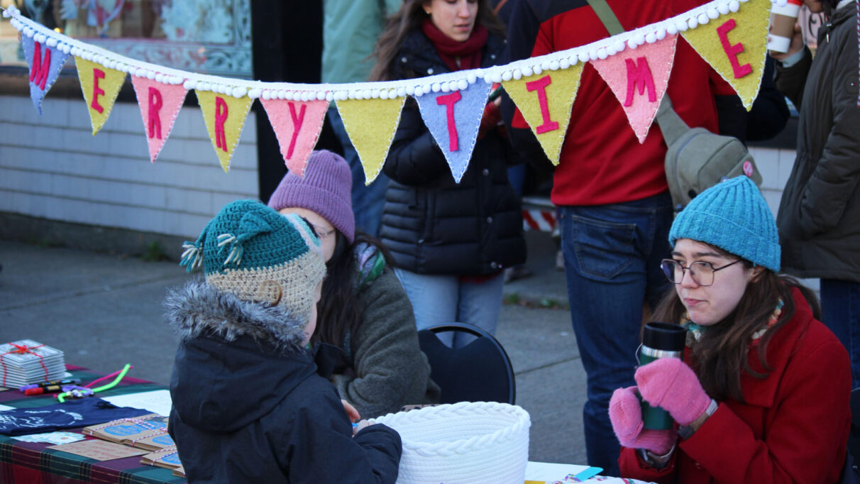 Adrianna Ciccone (left) and Isabelle Gagnon (right) sitting at Merry Time Music Company's booth during the Agricola Street Holiday Market.
