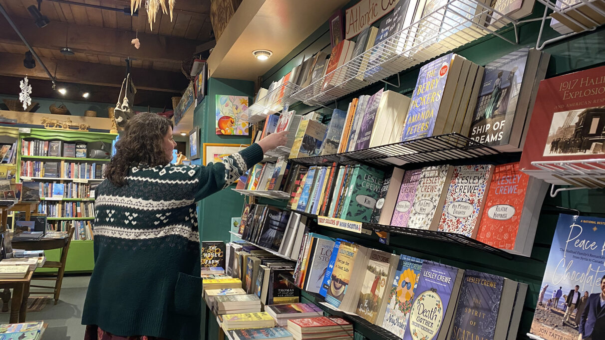 A woman in a black sweater stands shelving books in a bookstore.