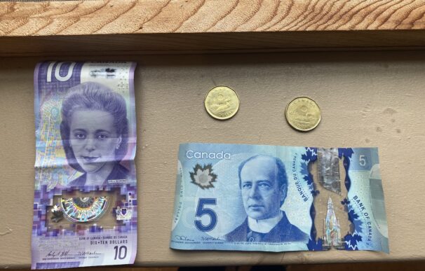 A $10 bill, $5, and two $1 coins sit on a wooden surface.