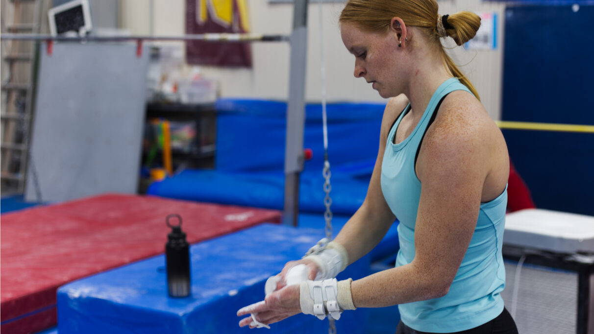 A woman with red hair in a bun and a blue tank top chalks her hands.