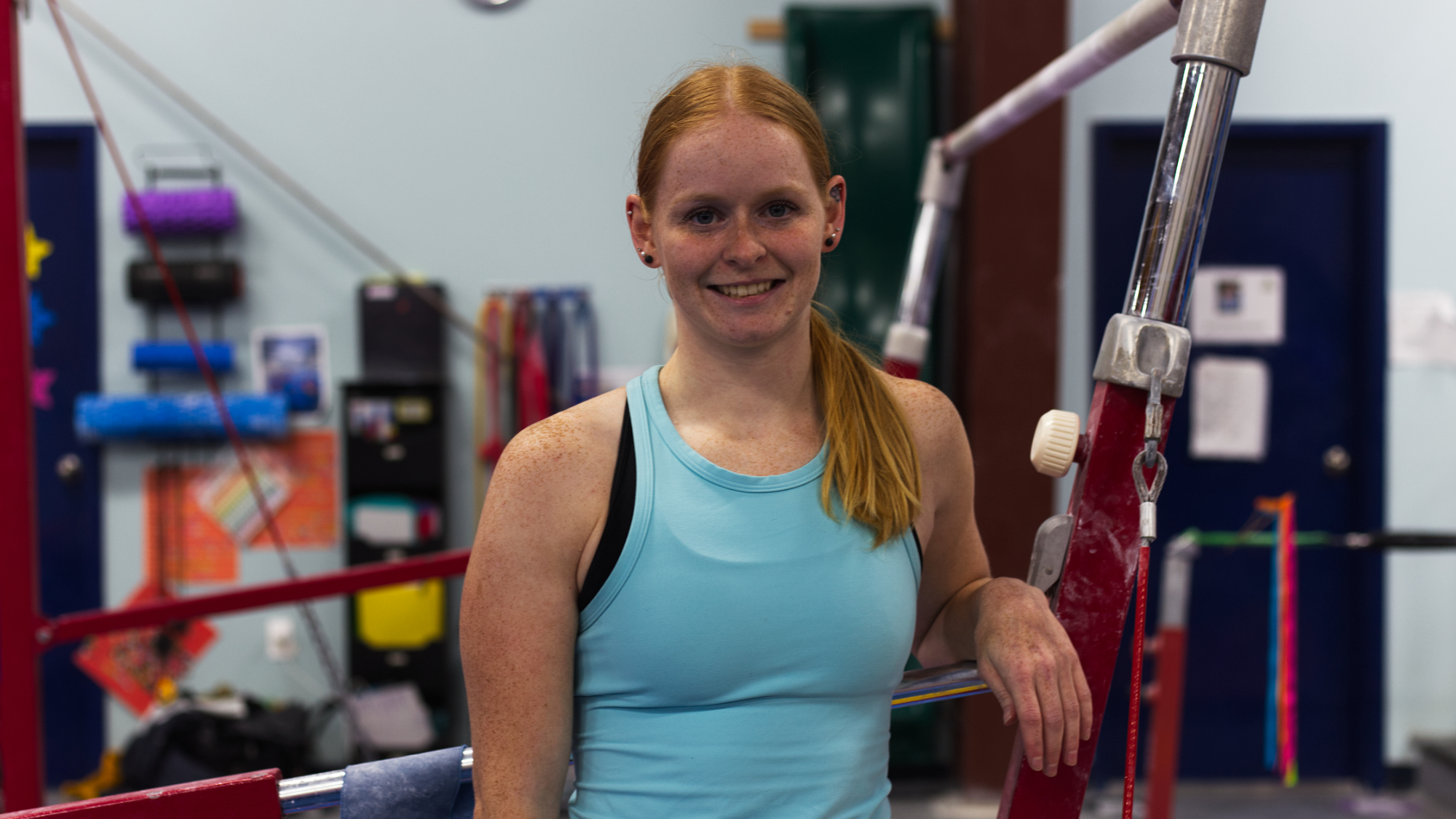A woman with red hair in a blue tank top smiles at the camera.