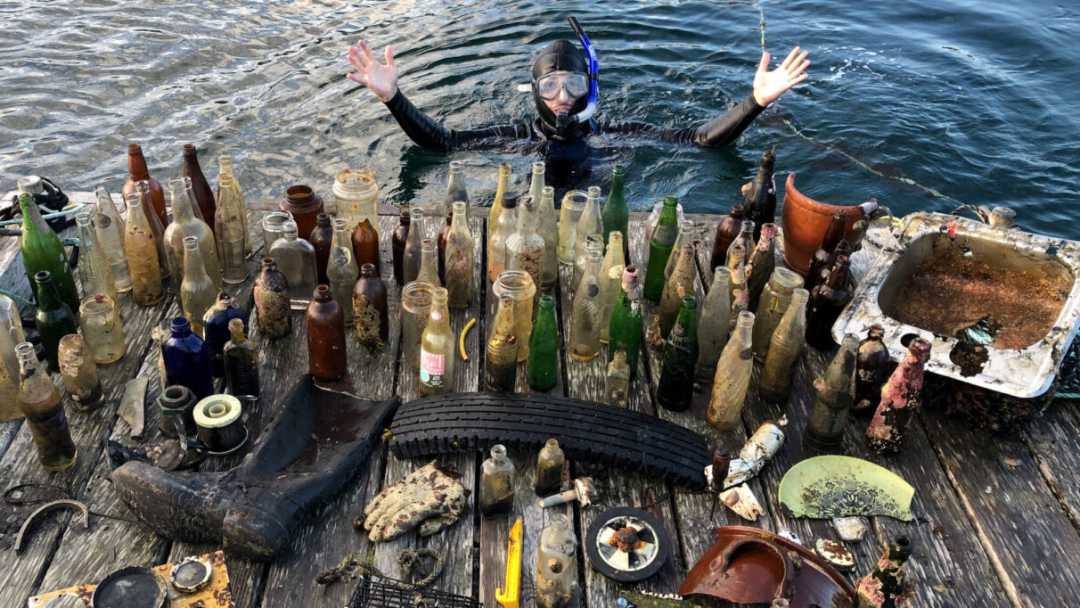 McMullen poses in the water with bottles and other finds from snorkeling.