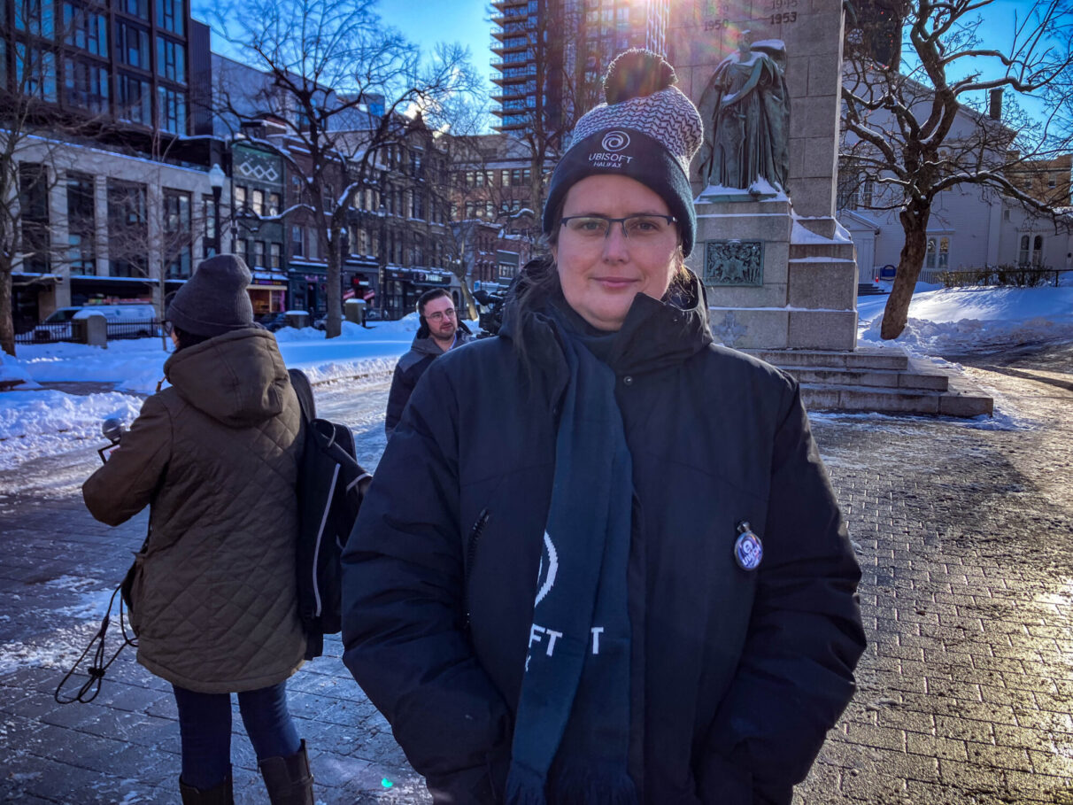 Britt Newstead poses for a portrait at Grand Parade. They are wearing a Ubisoft Halifax hat, scarf and union pin.