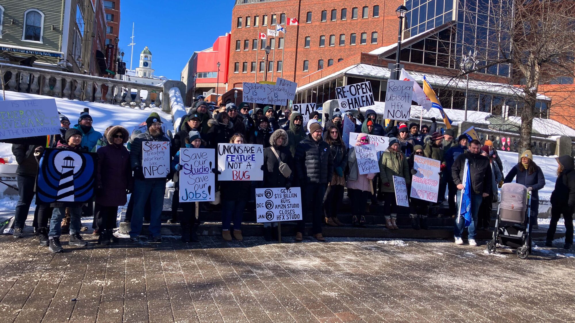 Former Ubisoft Halifax employees and supporters rally at Grand Parade holding protest signs.