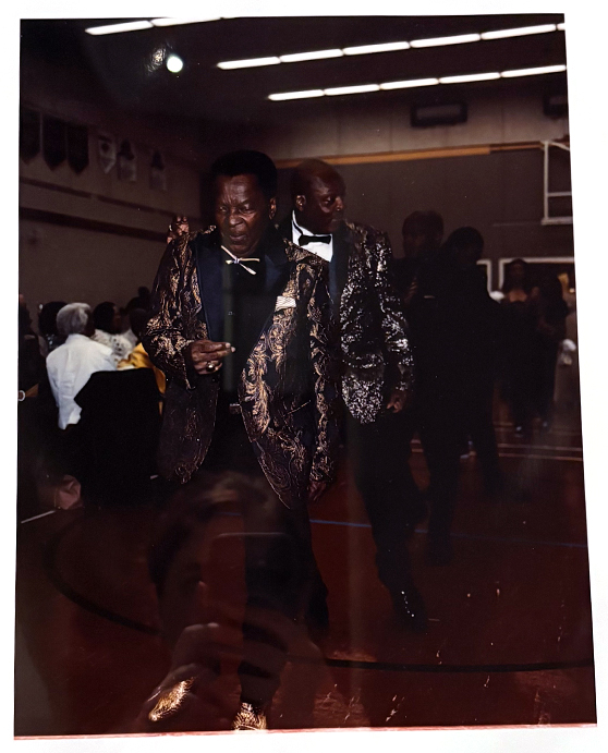 Two men dressed in gold and black tuxedos enter a wedding ceremony dancing.