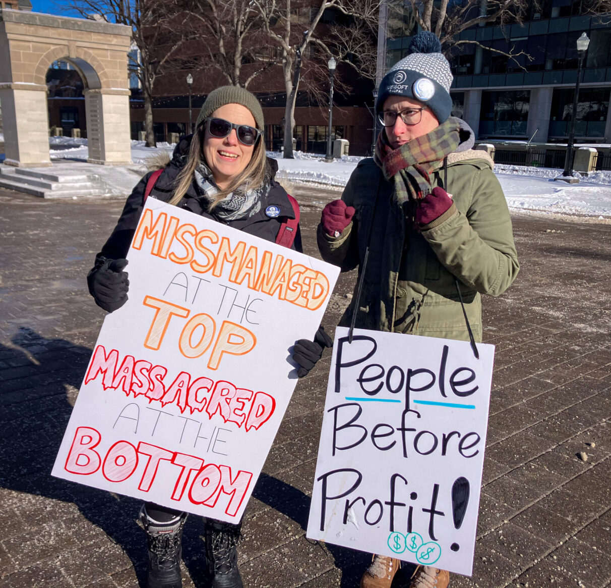 Camille Hunt (right) and Casey Davis rally at Grand Parade. Hanging from Hunt’s chest is a sign that reads “People before profit!”. Davis’ sign reads “Missmatched at the top, massacred at the bottom”.