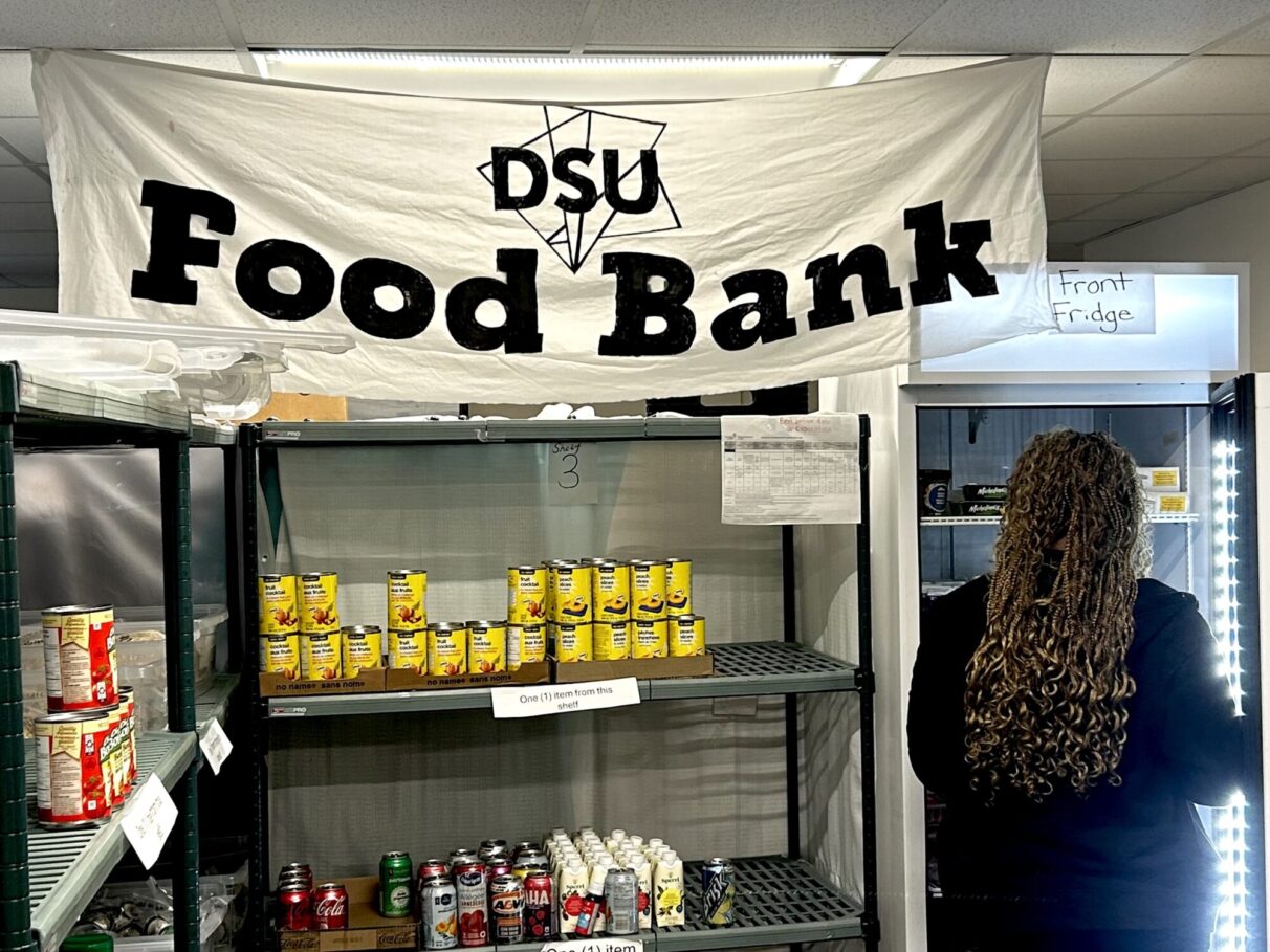 A student is opening the fridge containing frozen foods at the DSU Food Bank to grab some meals for the week.